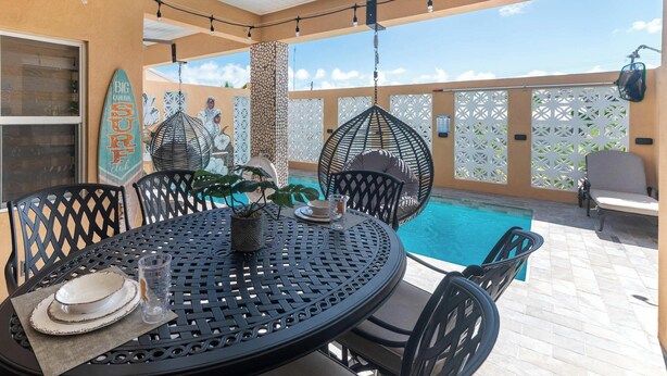 An outdoor patio with a round table, chairs, a hanging chair, and a pool. - Tropical House with Private Pool Near the Ocean (Oistins)