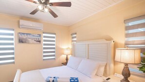 A hotel room with a bed, bedside lamps, a ceiling fan, and a window with blinds. - Tropical House with Private Pool Near the Ocean (Oistins)