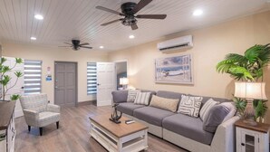 A living room with a sofa, armchairs, a coffee table, ceiling fans, an air conditioning unit, and a painting on the wall. - Tropical House with Private Pool Near the Ocean (Oistins)