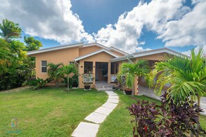 A two-story house with a covered porch, a lawn, and various potted plants. - Tropical House with Private Pool Near the Ocean (Oistins)