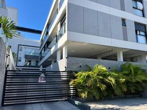 A modern building with a gated entrance, a covered parking area, and lush greenery. - Modern retreat in Novo Campeche, 100m from the beach! (Florianópolis)