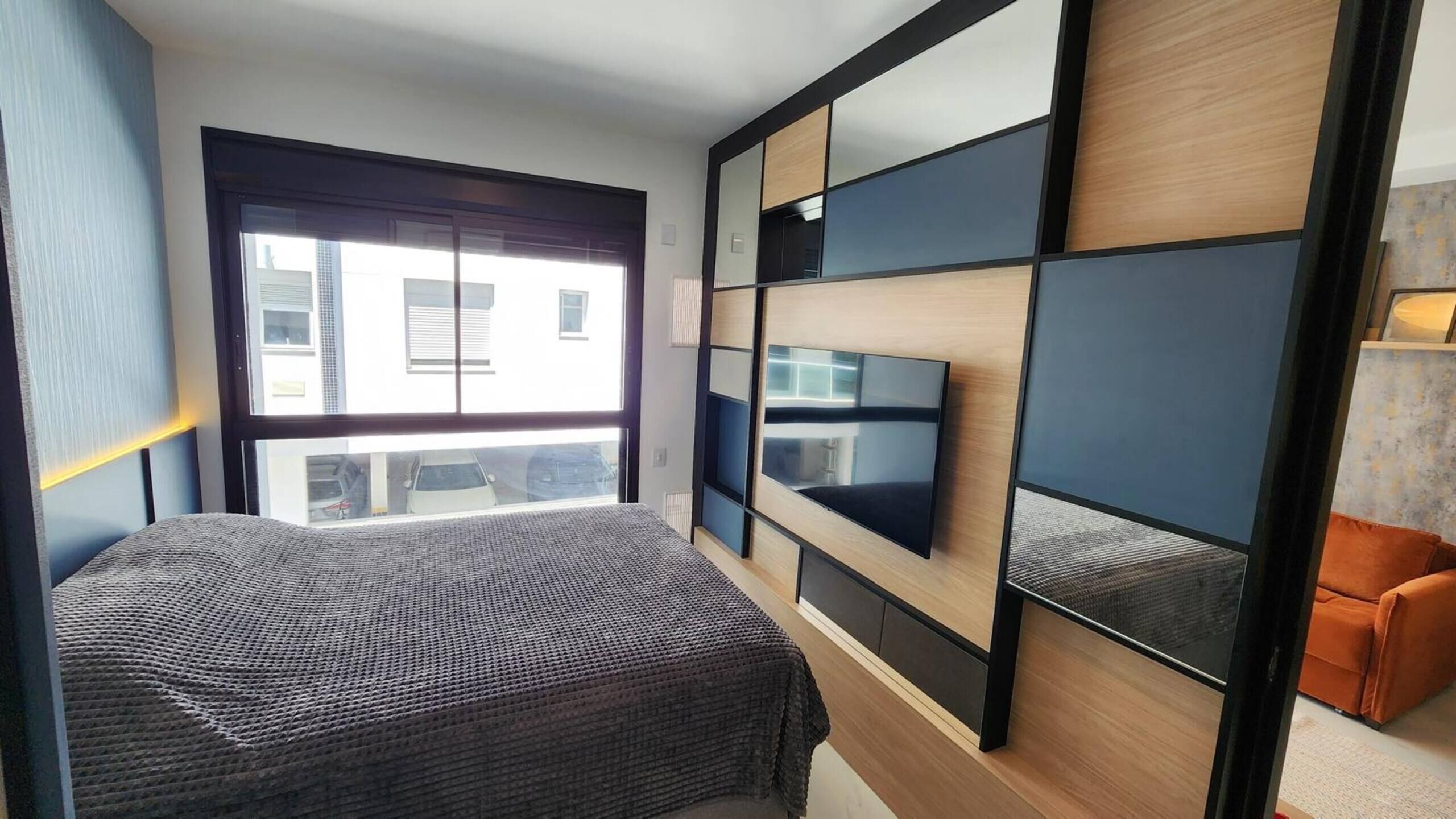 A modern hotel room with a large bed, a flat-screen TV mounted on the wall, and a view of the outside.