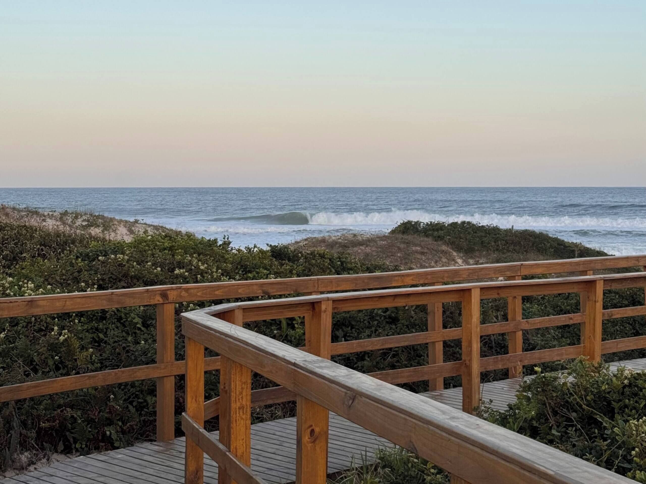 A wooden boardwalk leading to a beach with ocean waves in the background.