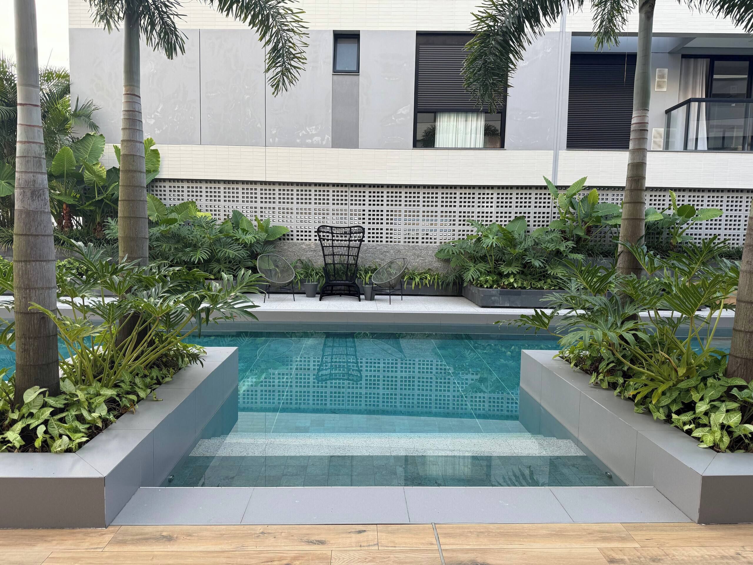 A modern outdoor pool area with a seating arrangement and lush greenery.