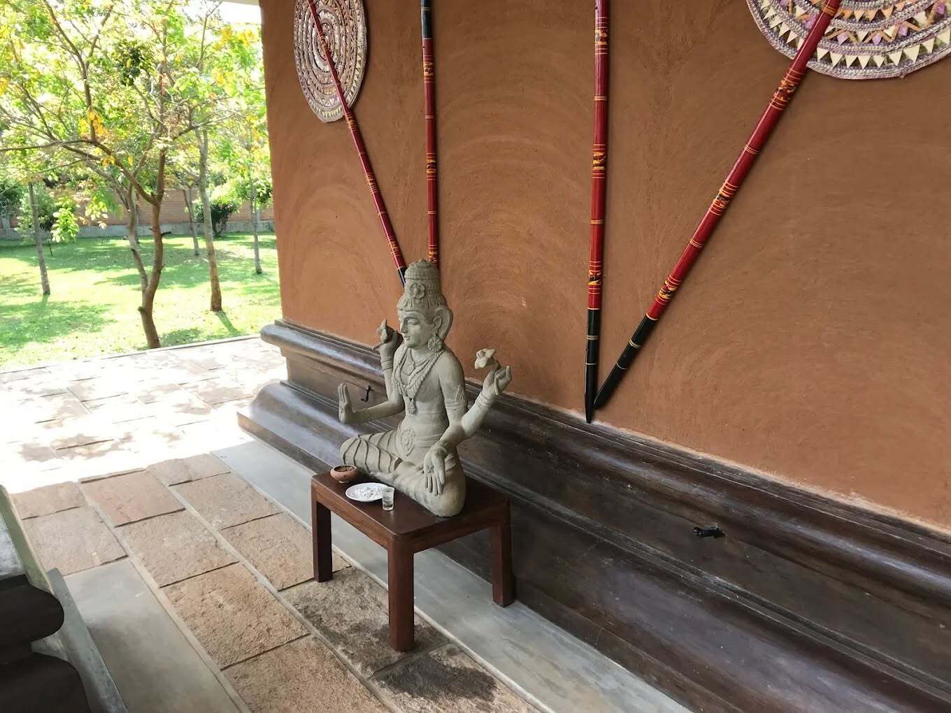 A statue of a deity on a bench in a covered area with a view of trees.
