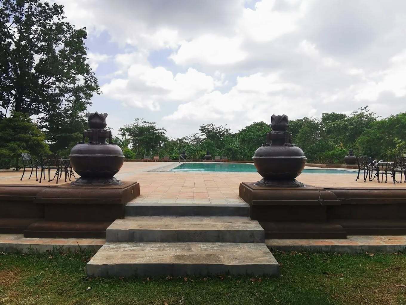 A pool area with steps leading to the water, surrounded by greenery and two large urn-like structures.