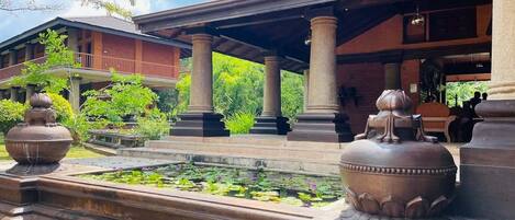 Un edificio tradicional con un porche cubierto, columnas y un estanque lleno de plantas de loto.