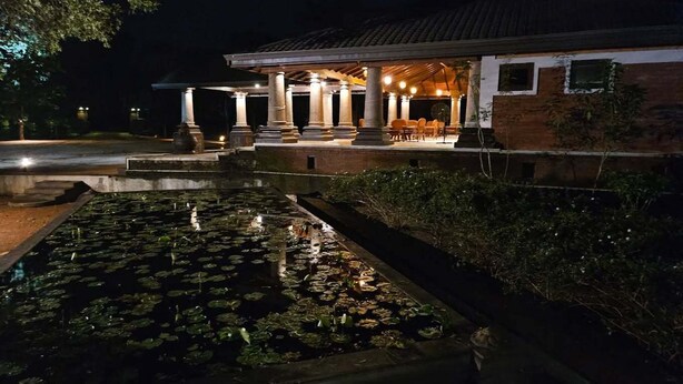 Un edificio con un espacio exterior cubierto, una fuente de agua con nenúfares y fachada de ladrillo.