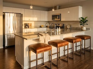 Une cuisine moderne dotée d’un îlot central, d’appareils électroménagers en acier inoxydable et de tabourets de bar.