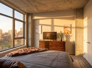 Une chambre à coucher avec un grand lit, une commode, un téléviseur et une vue sur le paysage urbain par la fenêtre.