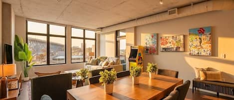 A spacious room with a large wooden table, comfortable seating, and large windows offering a view of the cityscape.