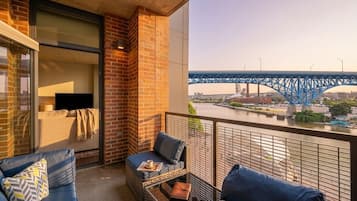 A balcony with a view of a blue bridge, wicker furniture, and a glass table.