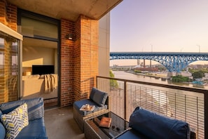 Un balcon donnant sur un pont bleu, avec des meubles en osier et une table en verre.
