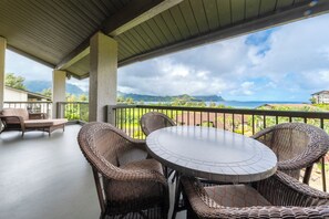 Un espace extérieur aménagé, abrité et doté de meubles en osier et d’une table ronde, offrant une vue panoramique sur les montagnes et l’océan.