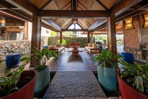 A covered outdoor seating area with wooden flooring, stone walls, and potted plants. - Kauai Escape at Award-Winning Bay Resort | Outdoor Swimming Pool | Parking (Princeville)