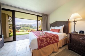 A hotel room with a bed, a nightstand, a lamp, and a view of the outdoors. - Kauai Escape at Award-Winning Bay Resort | Outdoor Swimming Pool | Parking (Princeville)