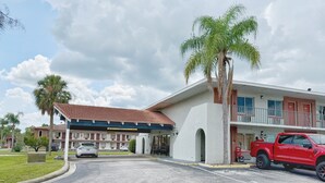 Un motel con área de estacionamiento techada, una camioneta roja y una palmera.