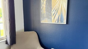 Habitación de esquina con un sillón estampado, pared azul y una obra de arte enmarcada.