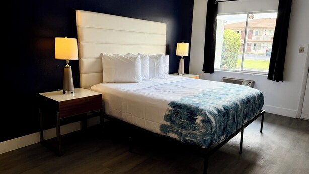 Habitación de hotel con cama, dos mesitas de noche, ventana con cortinas y vistas al exterior.