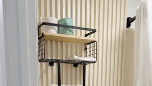 Un baño con inodoro, estante con toallas y cortina de ducha.
