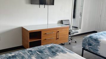 Habitación de hotel con dos camas, un aparador de madera, un televisor de pantalla plana, un espejo y una puerta.