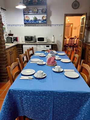 A dining area with a blue tablecloth, chairs, and a set table with plates, cups, and cutlery.