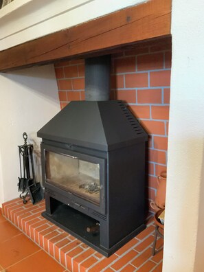 A wood-burning stove with a glass door, placed on a brick base, against a brick wall. - Quinta do Cota: The serenity of the Alentejo at this 3.3 h estate in Montemor o Novo (Montemor-o-Novo)