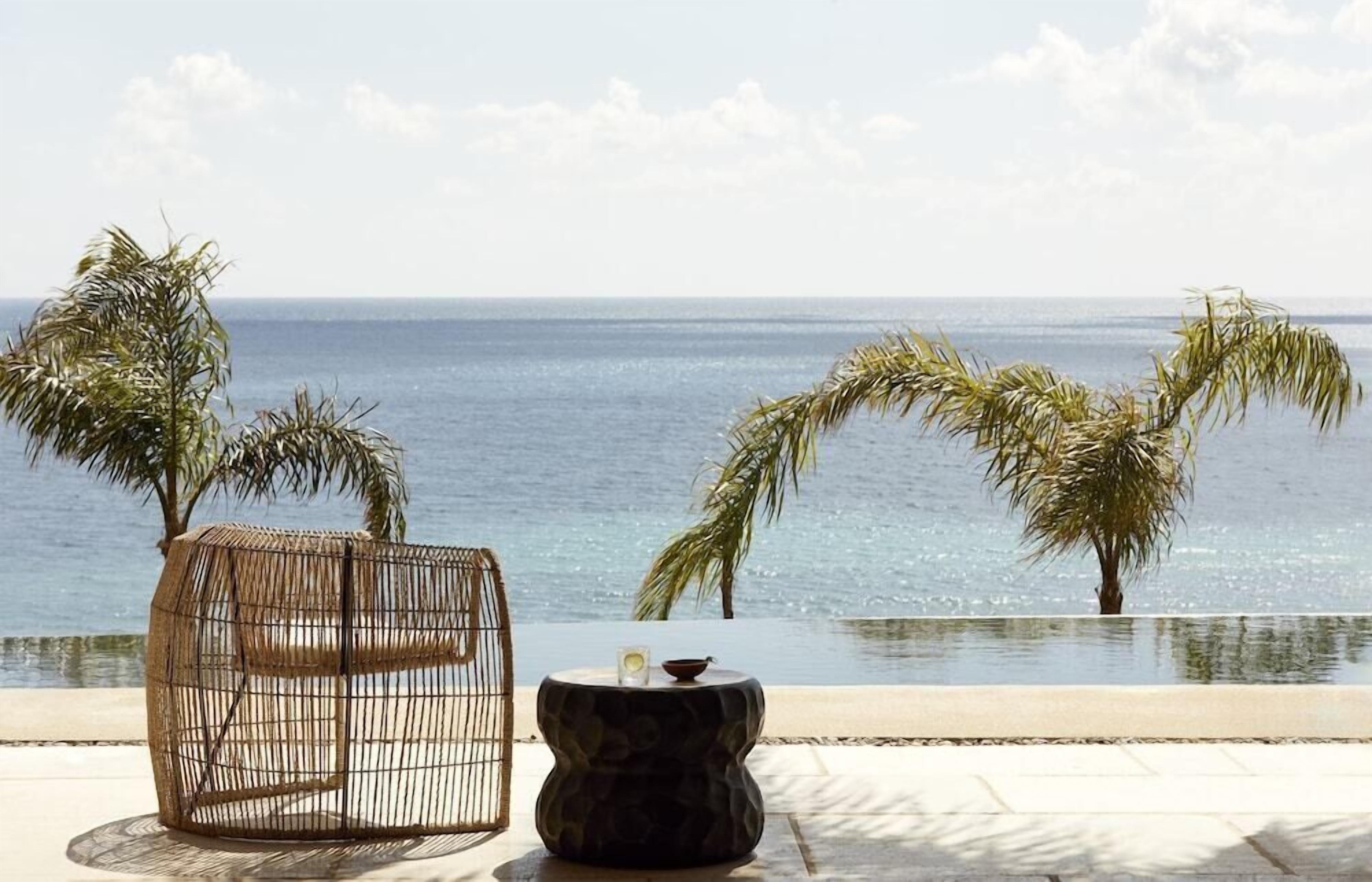 A beachside lounge with a wicker chair and a stone table, overlooking the sea.