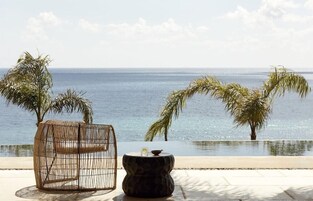 Un espacio de relax frente a la playa con una silla de mimbre y una mesa de piedra, con vistas al mar.