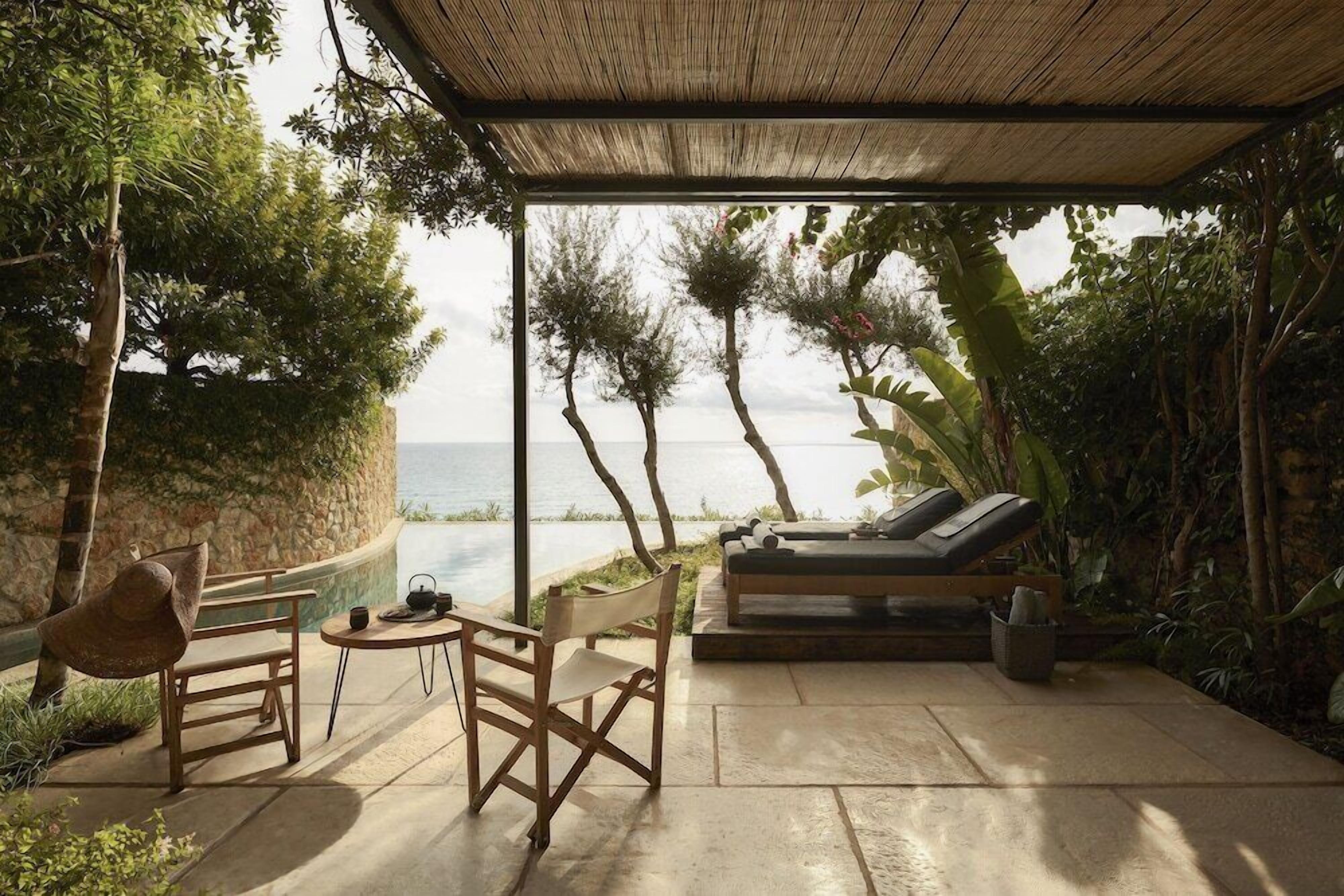 An outdoor seating area with a view of the sea, a covered structure, and a lounge chair.