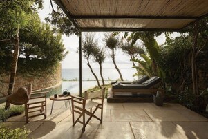 Un espacio de estar al aire libre con vista al mar, una estructura cubierta y una silla de descanso.
