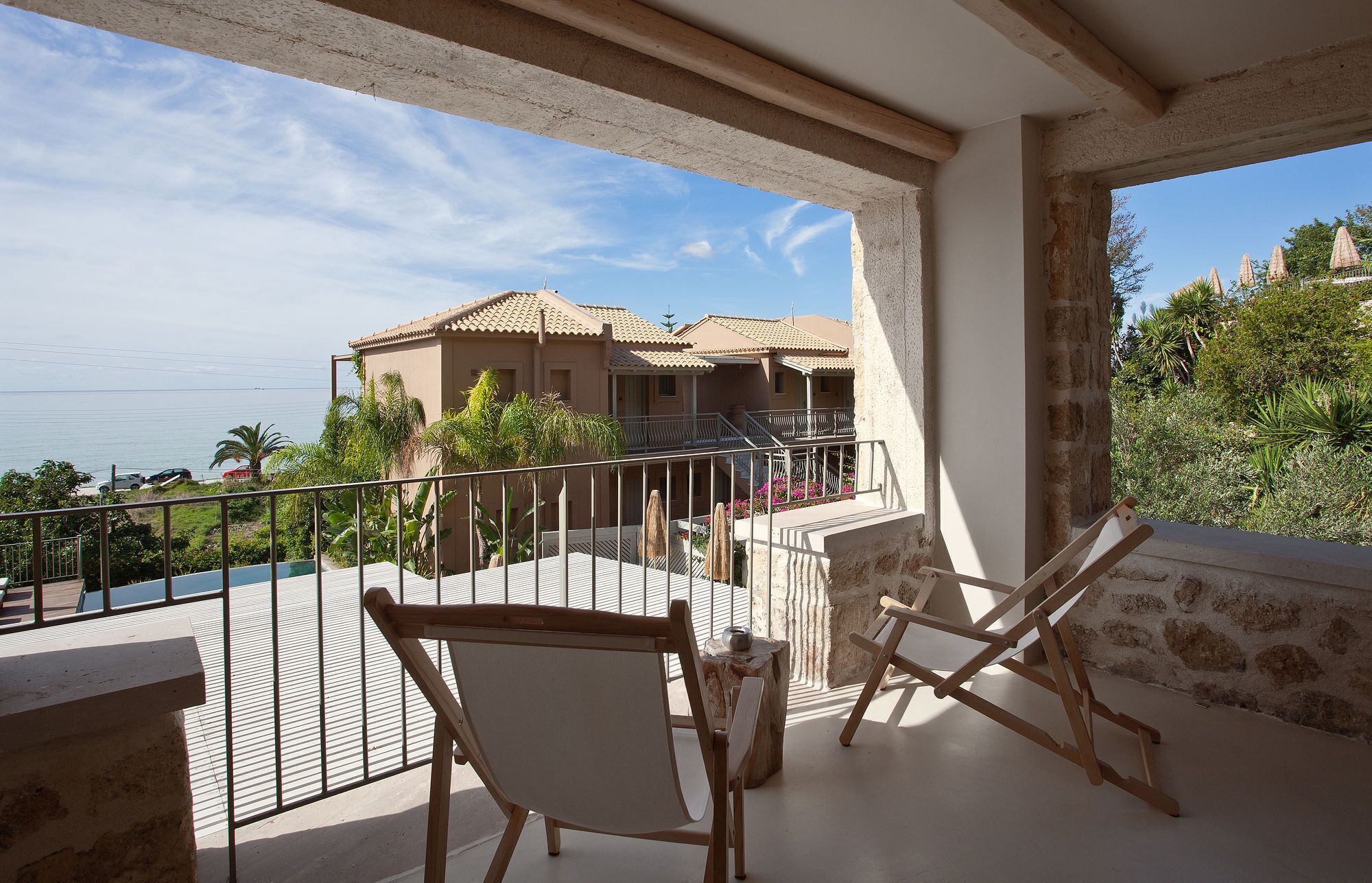 A balcony with two wooden chairs, a railing, and a view of a building with a tiled roof.