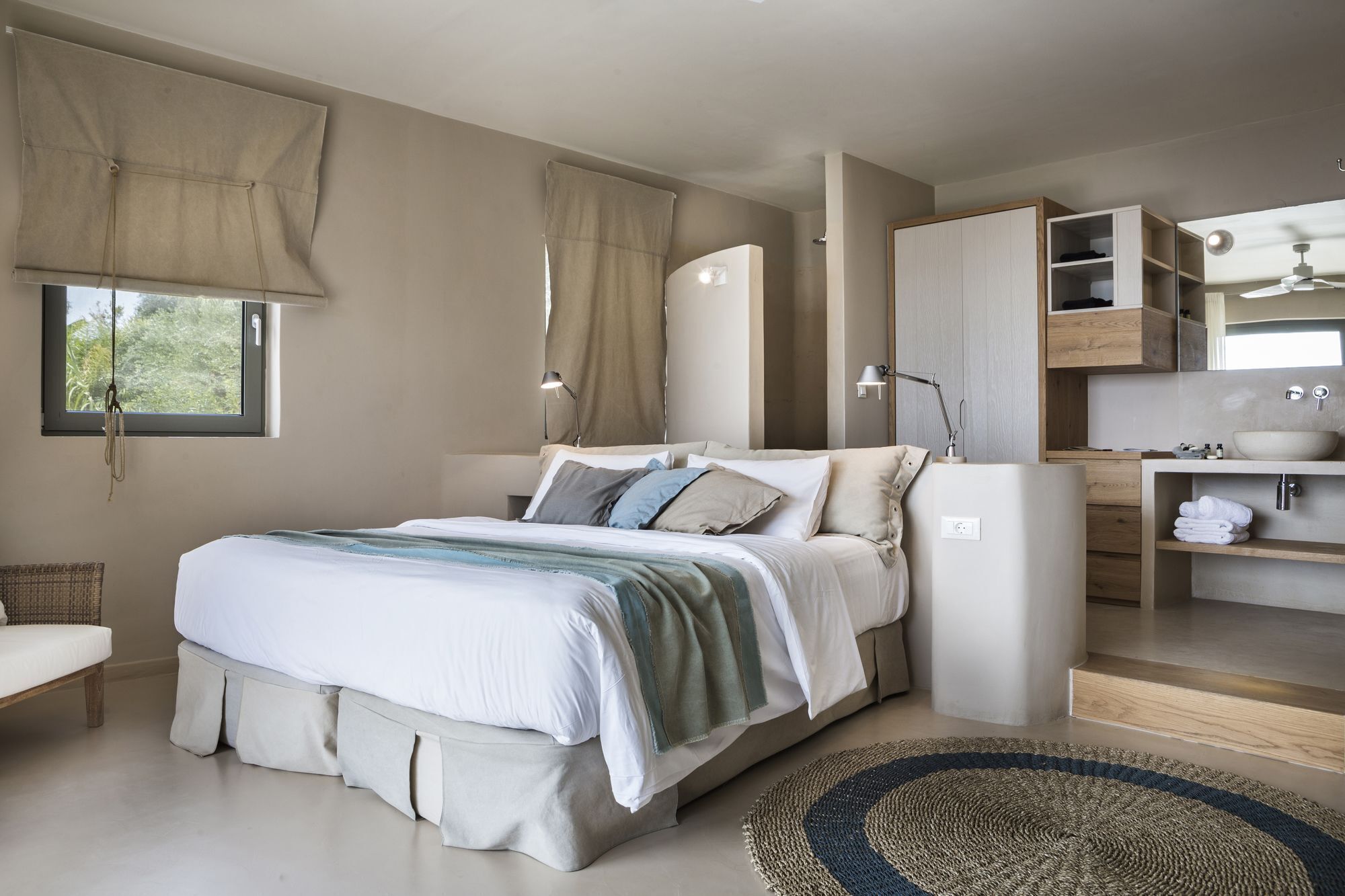 A modern bedroom with a bed, bedside lamps, a built-in wardrobe, and a bathroom with a sink and mirror.