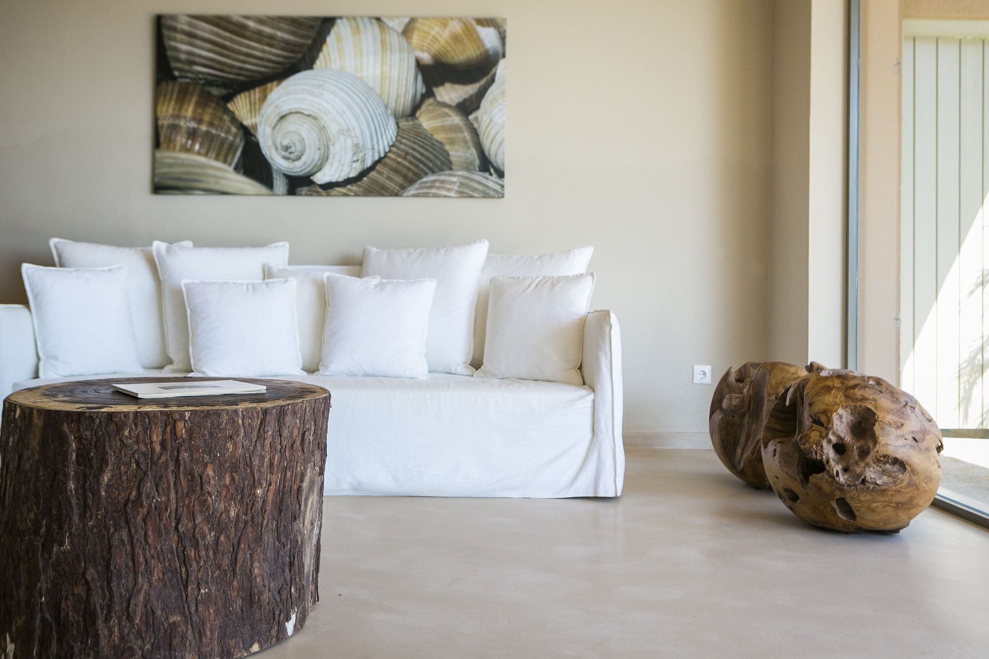 A living room with a white sofa, a round wooden coffee table, and a large sculpture.
