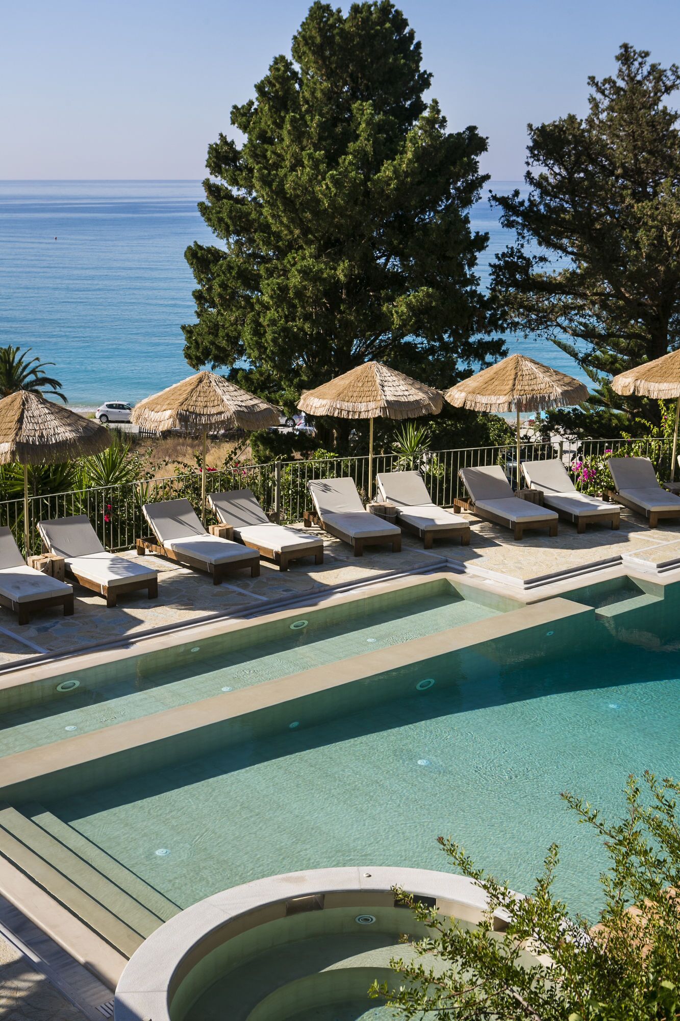 A pool area with lounge chairs and umbrellas, overlooking a body of water.