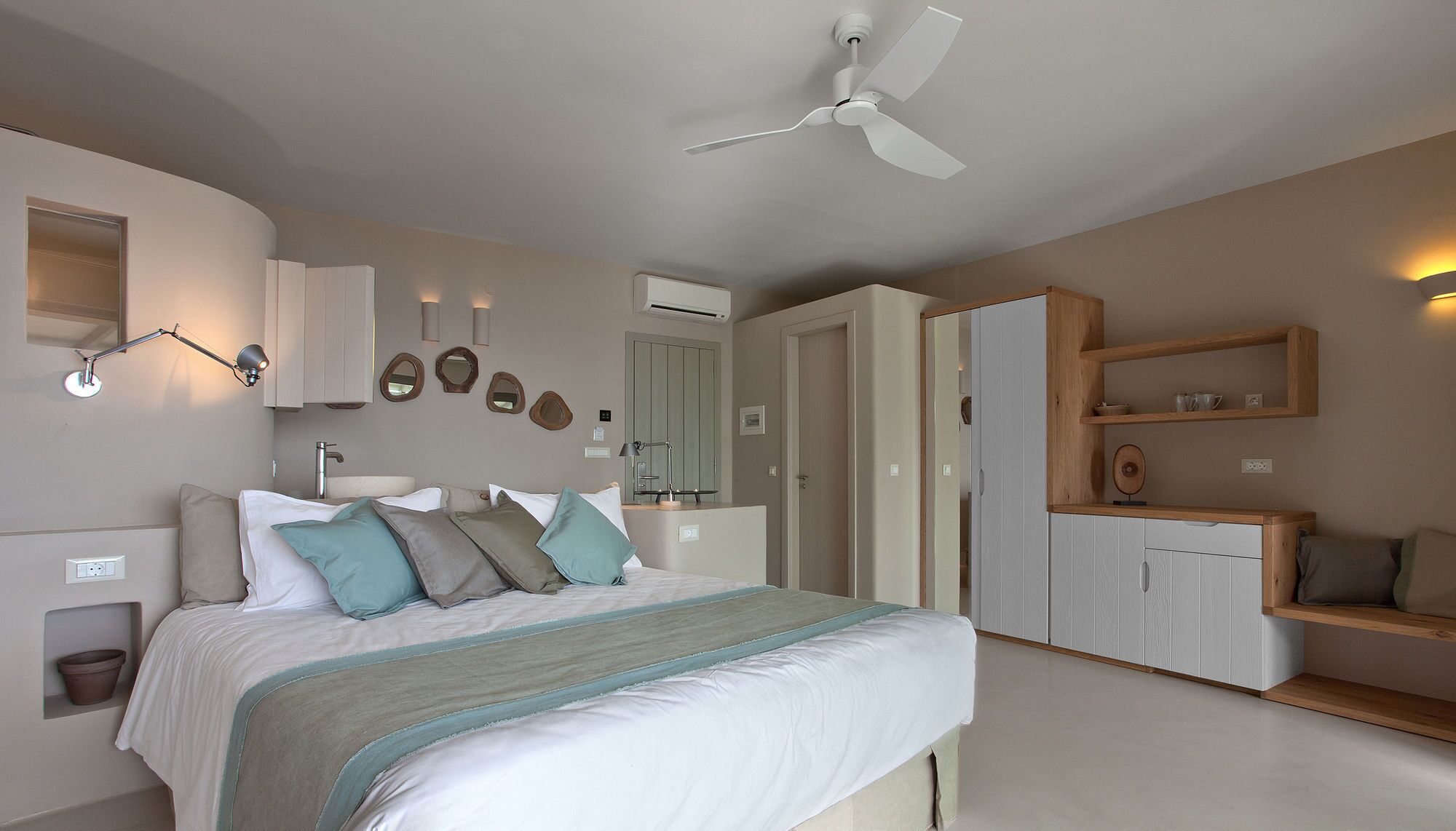 A bedroom with a bed, bedside tables, a wardrobe, a ceiling fan, and a bathroom with a sink and mirror.