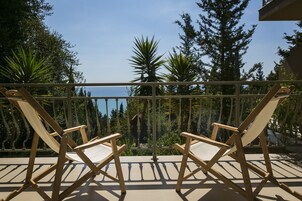 Dos sillones de madera en un balcón con barandilla, con vistas a un cuerpo de agua y un área boscosa.