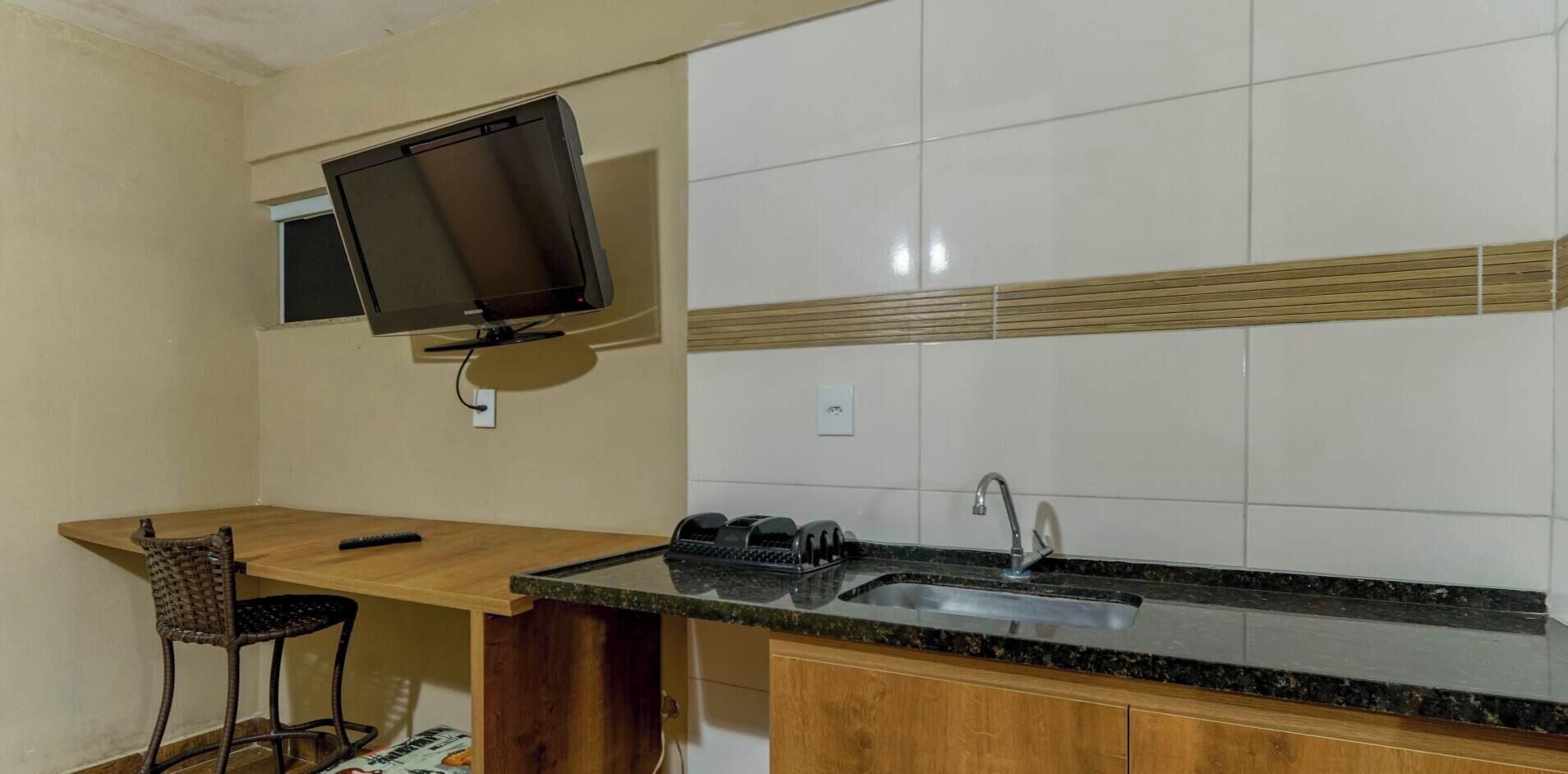 Une cuisine compacte avec un téléviseur à écran plat fixé au-dessus du comptoir, un évier et une chaise.