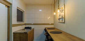 A compact kitchen with a sink, wooden cabinets, a window, and a dining area with a table and chairs. - Casa em Sao Pedro da Aldeia com Piscina e Jogos (São Pedro da Aldeia)