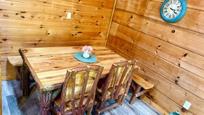 Een houten eettafel met stoelen, een klok aan de muur en een vaas met bloemen.