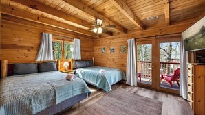 Een chalet met twee bedden, een plafondventilator en een balkon met rode stoelen.