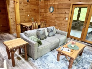 A cozy room with a grey sofa, two wooden tables, and a wooden dining table. - Bear Haven | Cozy Cabin•Hot Tub•Near Pigeon Forge (Pigeon Forge)