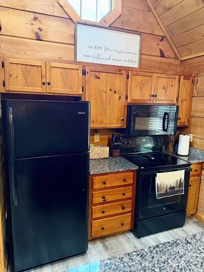 A kitchen with wooden cabinets, a black refrigerator, a stove, and a microwave. - Pet-Friendly Cabin Near Pigeon Forge & Gatlinburg (Pigeon Forge)