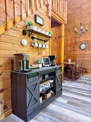 Ein rustikales Holzinterieur mit einer Kaffeestation, inklusive Tassen, einer Kaffeemaschine und einem Schild, das Kaffee, Tee und heiße Schokolade anbietet.