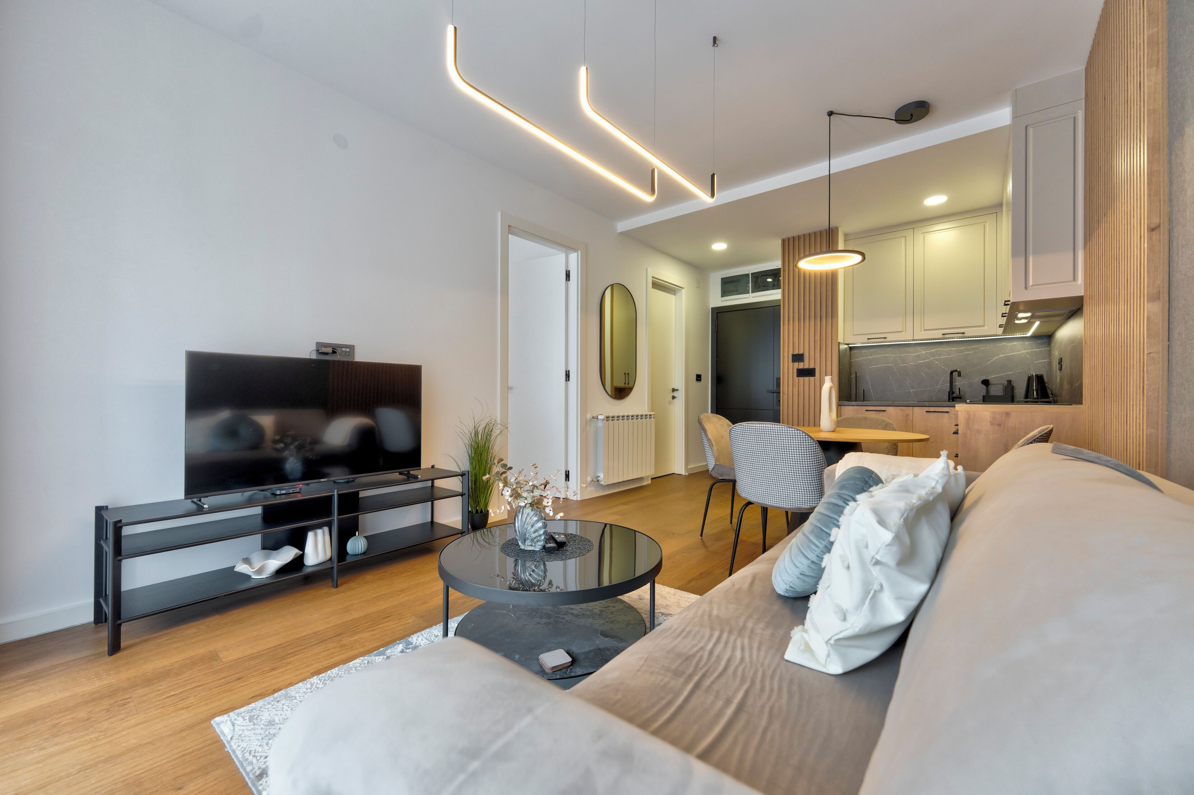 Una sala de estar moderna con una televisión de pantalla plana, un sofá, una mesa de centro y una zona de comedor con mesa y sillas.