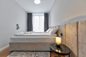 A modern hotel room with a bed, a bedside table with a lamp, a window with curtains, and a wall-mounted phone.