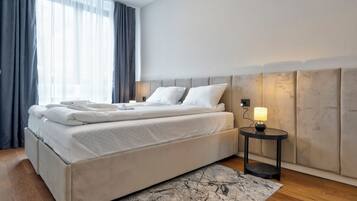 A modern hotel room with a large bed, a bedside table with a lamp, and a view of the outdoors through sheer curtains.