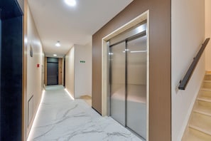A hallway with a marble floor, a wooden door, and a glass elevator.