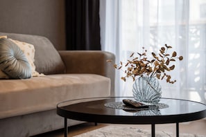 A modern living room with a sofa, a glass coffee table, and a vase with dried leaves.