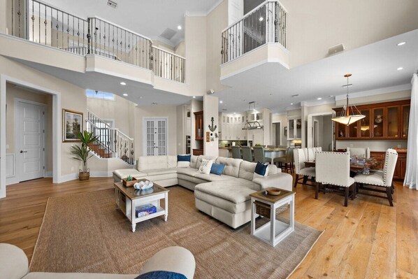 A spacious living area with a large sectional sofa, a dining table with chairs, and a kitchen in the background.